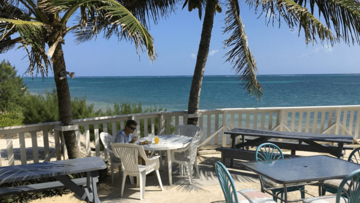 picture of man eating by himself at a table with sea in background